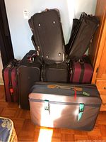 Group photo showing multiple pieces of soft-sided luggage stacked, including navy blue with straps and black and maroon suitcases.