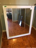 Front view of the large mirror with white painted wooden frame on parquet floor with reflection of room.
