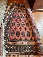 Partially rolled Persian rug showing the main field pattern with black oval medallions on a pink background and lateral fringes.