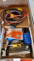 Overall view of Campbell Hausfeld pneumatic nailer with air hose and staples inside an open box.