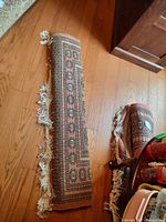 Partial rolled-up view of coral and dark patterned synthetic rug with fringed white tassels on oak floor.