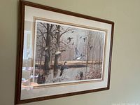 Full view of the framed print showing a woodland scene with flying ducks and trees, framed with a dark wooden frame and cream mat.