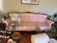 Full view of pink tufted sofa with carved wood frame, showing cushions and some surrounding items.