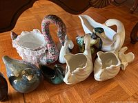 Wide view showing group of swan and duck figurines on wooden floor, various materials and sizes visible.