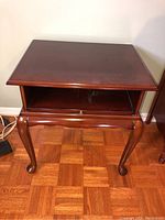 Wood table open view showing pull-out shelf and curved legs on parquet floor.