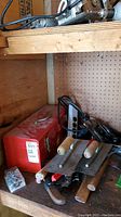 Wooden shelf with red metal toolbox, electrical outlet, two drywall floats, and other hand tools arranged around the toolbox.