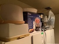 Photo of stacked Tupperware storage containers and boxed Oster digital food steamer with other kitchen appliances in the background.