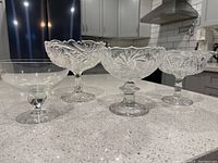 Four vintage glass candy dishes in a row on countertop.