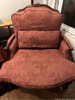Close-up of burgundy floral patterned armchair showing carved wooden frame and cushions
