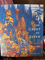 Cover of 'The Group of Seven' art book showing a colorful landscape painting with autumnal foliage and rock formations.