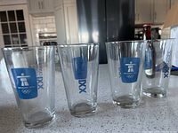 Four clear pint glasses with blue Vancouver 2010 Winter Olympics logo and Olympic rings printed on each.