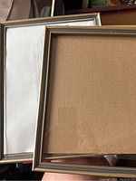 Two silver-tone picture frames showing front sides with cardboard backing and one frame with glass or mirror surface visible.