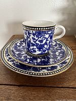 Photo of stacked cup, saucer, and sandwich plate showing the cobalt blue floral chintz design with gold accents and white dotted border.