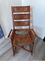 Front view of Costa Rican wooden rocking chair with three leather backrest panels and leather seat showing hand-tooled designs.