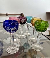 Photo showing all six colored long stem aperitif glasses in blue, pink, purple, turquoise, yellow, and green. Showing cut crystal, faceted stems and radial feet.