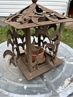 Side angle of one rustic metal garden lantern showing leaf cut-out design and terracotta pot inside
