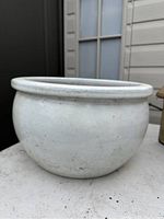 Close-up of a large round white clay planter showing slight dirt and speckling on surface with drainage hole visible inside.