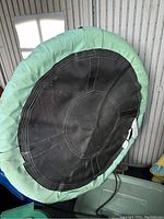 Round swing close-up showing black seat with green fabric padding surrounding the seat.