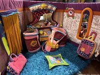 Photo of a colorful fabric room setup with doll furniture including a bed, a vanity, suitcases, lamps and a mirror, featuring purple, orange, pink, and blue colors.