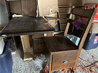 Frontal side view of old wooden student desk attached to chair with drawer beneath seat and boxes stacked in background