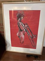 Framed charcoal drawing of a nude trombone player on red background by Clare Moore.