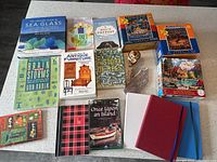 Photo showing assortment of eight books and four journals arranged on a table, plus a small pottery item in plastic wrapping