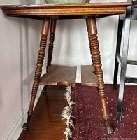 Side view of a vintage wooden claw foot table focusing on turned legs and castor wheels, showing wear and wood discoloration.
