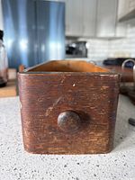 Front view of old wooden sewing machine drawer showing round knob and wood grain.