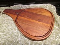 Vintage Adams walnut cutting board in paddle shape showing overall front with rich wood grain, leather hanging thong, and magnetic holder by the handle.