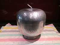 Front view showing the rounded apple shape with hammered aluminum texture and attached lid with stem handle.