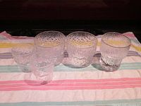 Front view of five clear textured drinking glasses on a striped cloth, showing group and size variation.