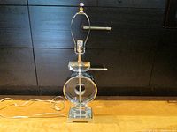 Full view of contemporary decorative table lamp showing chrome base, acrylic spinning medallion, lamp socket and finial.