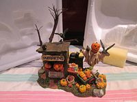 Full view of the Department 56 Pumpkin Stand figurine showing wooden stand with pumpkins, scarecrow with jack-o'-lantern head, black crows, and surrounding pumpkins and cart.