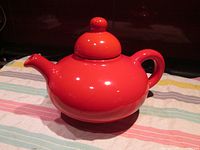 Front side view of red Flowerdale Hayhoe Beauceware teapot model 3320, large size on striped cloth.