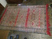 Full view of the handwoven flat weave Moroccan area rug laid out on a stone floor, showing red fringed end and geometric multicolor pattern.