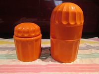 Two orange kitchen tools side-by-side, the smaller grater and larger citrus juicer, showing the overall shape and color