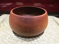 Side view of the solid teak wood bowl showing round smooth shape with visible wood grain and polished surface.