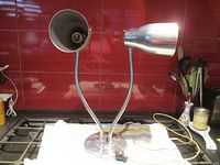 Full view of double necked gooseneck table lamp on kitchen counter showing both lamp heads, gooseneck arms, base, power cord and plug.