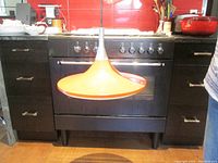 Front view of orange metal witch hat pendant light hanging in kitchen setting. Shows shape and color.