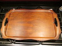 Top view of rectangular teak serving tray on stove, showing ruffled edges and handle cut-outs