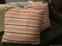 Two 24-inch square cushions with red, beige, and gray horizontal striped covers on a gray sofa.
