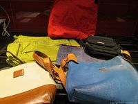 Group of 6 purses and bags stacked and arranged showing various colors and materials including leather and nylon