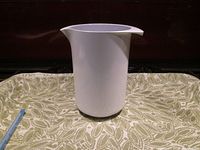 White Rosti pitcher shown from the side to display shape and size, placed on a patterned cloth surface.