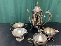 Photo of four silver plated items against green background showing reflective surfaces and decorative handles and finials.