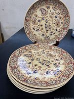 Photo of five stacked ceramic dinner plates with a traditional Portuguese floral and paisley pattern in blue, red, and brown on cream background, showing decorative rims and intricate details.