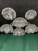 Top view of six different cut glass bowls laid out on black fabric showing varied detailed patterns and shapes.