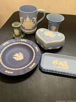 Six Wedgwood JasperWare pieces displayed on black surface showing various shades of blue and green items with white relief decoration.