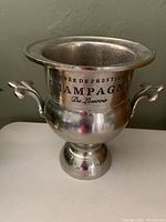 Front full view of silver champagne ice bucket with decorative handles and black printed text.