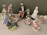 Front view of the nine vintage figurines showing details of hand-painted colors and characters including a seated man, Victorian figures, praying girl, and animals in costumes.