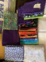Photo showing assorted fabric yardage pieces with different colors and prints including purple solids, batik, floral, geometric, and animal patterns.